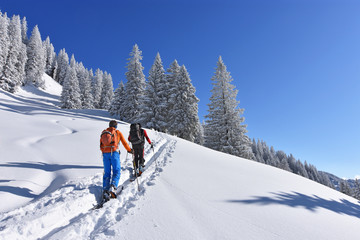 Two skiers with backpacks on the way in a deeply snow-covered landscape in the mountains with...