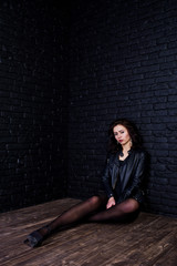 Studio portrait of sexy brunette girl in black leather jacket against brick wall.