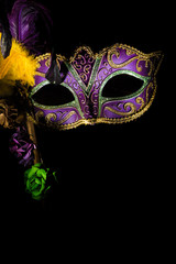 A purple mardi gras or venitian mask with feathers and flowers on a black background with copy space © jaflippo