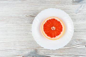 A fresh grapefruit on a white plate on a wooden background