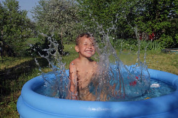 the little boy is very emotionally playing and laughing laps with the water in the children's pool of blue.