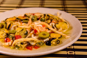 Ceramic plate with different sea food and olives on a bamboo mat