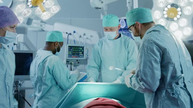 Diverse Team of Professional Surgeons Performing Invasive Surgery on a Patient in the Hospital Operating Room.  Shot on RED EPIC-W 8K Helium Cinema Camera.
