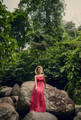 A girl in a red dress is sitting on a rock. Traveling in the jungle.