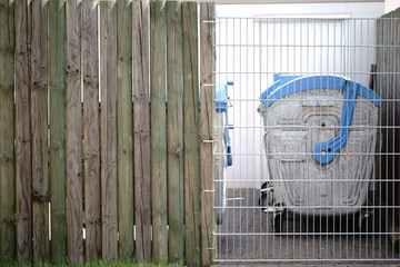 Private Abfallcontainer / In einer Reihe angeordnete Mülltonnen stehen hinter einem Gitterzaun in...