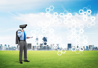 Camera headed man standing on green grass against modern cityscape