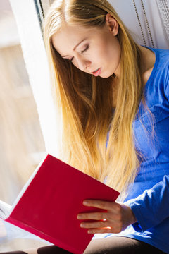 Woman sitting on window sill reading book at home