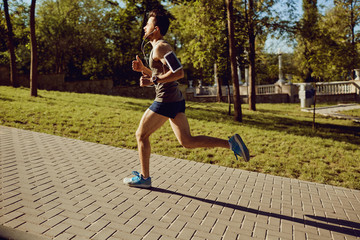 A male runner runs along the road to the park in the summer.