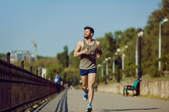 A male runner runs along the road to the park in the summer.