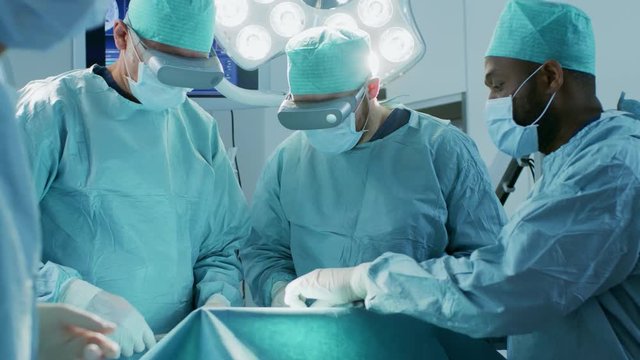 Surgeons Wearing Augmented Reality Glasses Perform State of the Art Mixed Reality Surgery in High Tech Hospital. Doctors and Assistants Working in Operating Room.