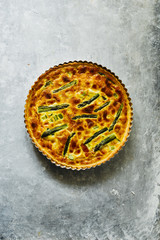 Quiche with green asparagus
, egg, cream, scamorza cheese and spec ham, round shaped on an aluminium mold, top view over a gray emerald  board.