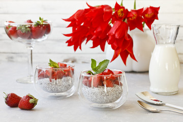 Close-up of sweet fresh strawberry meal in bowls with beautiful red tulip flowers on gray background. Top view, selective focus