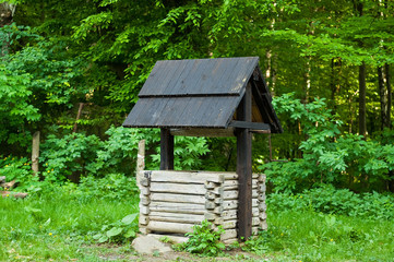 Fototapeta na wymiar genuine wooden well with black roof in the forest, concept of authentic objects in the wild, copy space, close-up