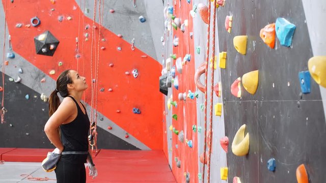 Beautiful young woman starts to climbing big artificial wall.