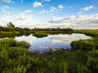 Obraz na płótnie Canvas A view of the pampa biome, clouds reflecting on small pond - Uruguaiana, Brazil