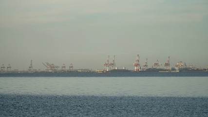 Industrial cargo port with ships and cranes. View of the cargo port and container terminal. Container cranes in Manila Bay. Cargo ship in industrial port. Manila, Philippines.