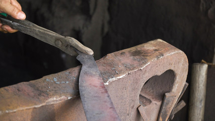 Blacksmith working metal with hammer on the anvil in the forge. hammer forging hot iron at anvil. Blacksmiths make machete. Hands of the smith by the work. Philippines.