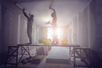 Workers are installing ceiling from wooden scaffolding platform in apartment is under construction,...