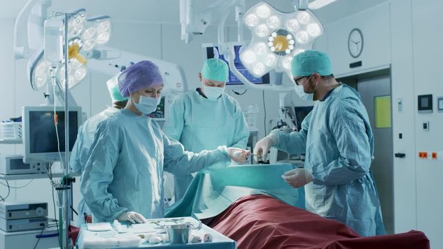 Diverse Team of Professional surgeon, Assistants and Nurses Performing Invasive Surgery on a Patient in the Hospital Operating Room. Surgeons Talk. Shot on RED EPIC-W 8K Helium Cinema Camera.