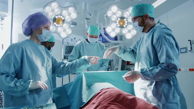 Gliding Shot of Diverse Team of Professional Surgeons Performing Invasive Surgery on a Patient in the Hospital Operating Room.  Shot on RED EPIC-W 8K Helium Cinema Camera.