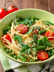 Spaghetti pasta with green beans, peas, cherry tomatoes, parsley and parmesan cheese on wooden table