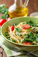 Spaghetti pasta with green beans, peas, cherry tomatoes, parsley and parmesan cheese on wooden table