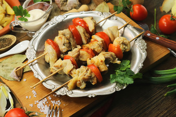 fried chicken meat with tomatoes on wooden sticks. Barbecue with vegetables on a wooden background.