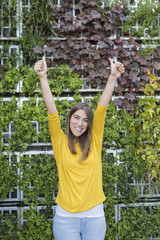 portrait outdoors of a beautiful young woman with thumbs up and smiling. Wearing a yellow casual shirt over green background. LIfestyle and fun.