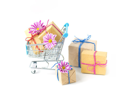 Creative concept of shopping trolley with wrapped gifts and flowers on light background. 