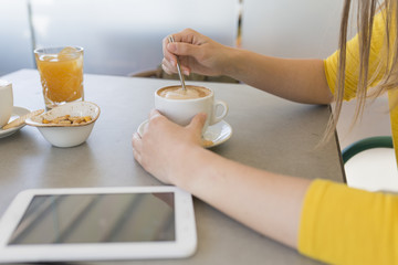 young woman having breakfast in a restaurant. Coffee, orange juice and tablet on the table. Daytime, lifestyle