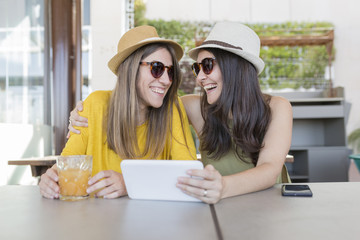 two beautiful women having breakfast in a restaurant. They are laughing and searching information on a tablet. Indoors lifestyle and friendship concept