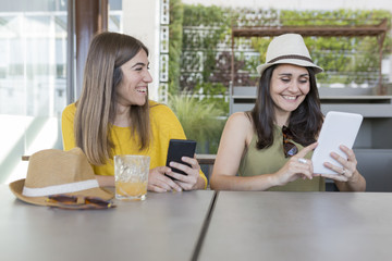 two beautiful women having breakfast in a restaurant. They are laughing and searching information on a tablet. Indoors lifestyle and friendship concept