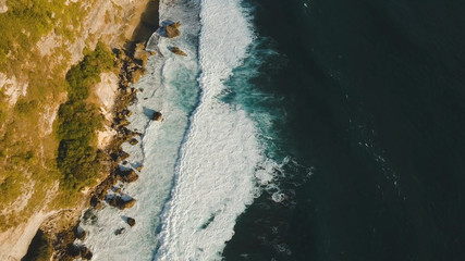 Aerial view of rocky coast with surf the waves off the at sunset, Bali,Indonesia, Pura Uluwatu cliff. Waves crushing rocky shore. Seascape, rocks, ocean. Travel concept.