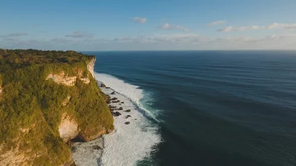 Aerial view of sea rocky coast with surf the waves, Bali, Indonesia, Pura Uluwatu cliff. Waves crushing rocky shore. Seascape, rocks, ocean. Travel concept.