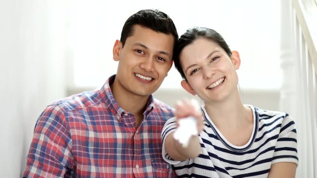 Young Couple Sitting On Stairs Holding Keys To New Home Shot In Slow Motion