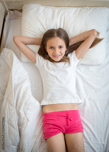 "Portrait of beautiful smiling girl in pajamas lying on bed and looking