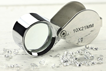 brilliant cut diamonds with folding magnifier on wooden background