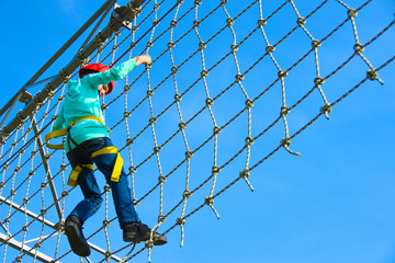 Teenager boy moves the vertical grid on the obstacle course in the amusement park, outdoor activities, rock climbing, danger, training, height, fear, copy space
