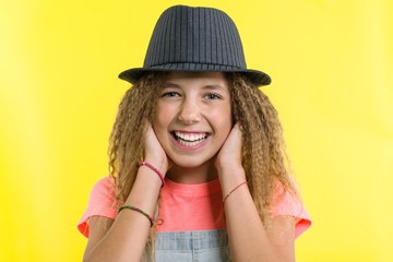 Portrait of laughing teen girl in hat, looking at the camera over yellow background.