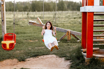 Little girl is swinging at a playground when the sun is setting. Happiness and family concept