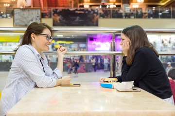 Communication of adult mother and teenage girl. Background table in cafe, in the shopping mall entertainment center.
