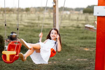 Little girl is swinging at a playground when the sun is setting. Happiness and family concept