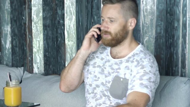 Angry man talking on cellphone sitting on sofa at home
