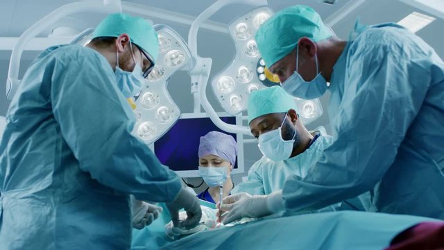 Diverse Team of Professional surgeon,  Assistants and Nurses Performing Invasive Surgery on a Patient in the Hospital Operating Room. Surgeons Talk and Use Instruments. Shot on RED EPIC-W 8K.
