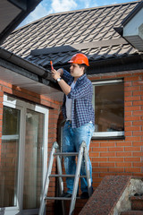 Young male builder standing on stepladder and repairing rooftop
