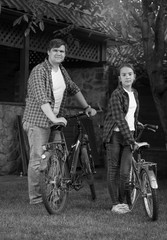Black and white photo of young man with teenage daughter posing with bicycles at house backyard