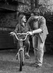 Black and white photo of young man teaching his daughter riding bicycle at park