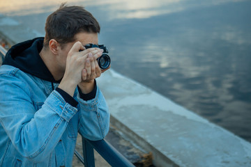 Obraz premium A man in a denim jacket with a vintage film camera at sunset