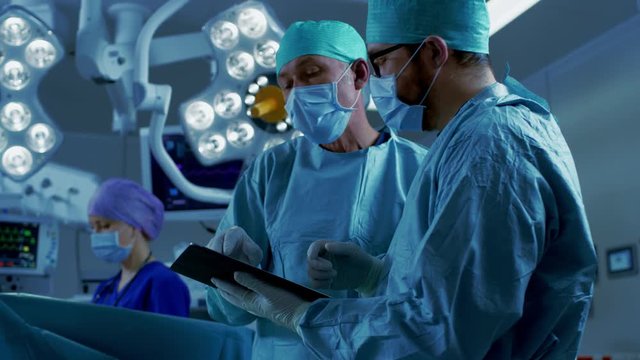 Two Professional Surgeons Use Digital Tablet Computer while Standing. Shot on RED EPIC-W 8K Helium Cinema Camera.