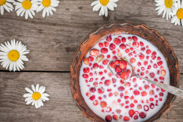 Sweet wild strawberries in plate with chamomile on wooden background, top view.